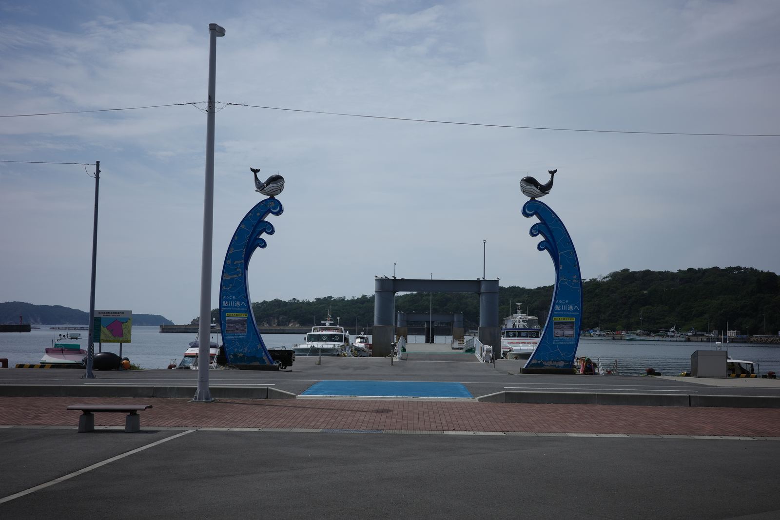 クジラの載った青い波形のモニュメントが左右に立つ鮎川港の発着場。奥に停泊する船