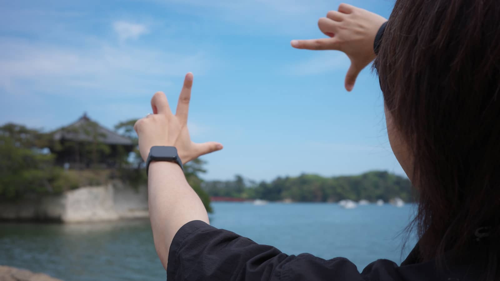 松島湾を背に、両手の指で四角いフレームを作って構図を確かめている