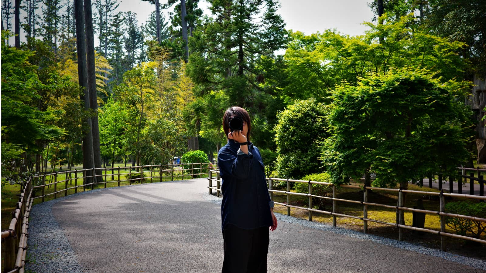 木々に囲まれた参道で、カメラを構えて撮影するNaofumi