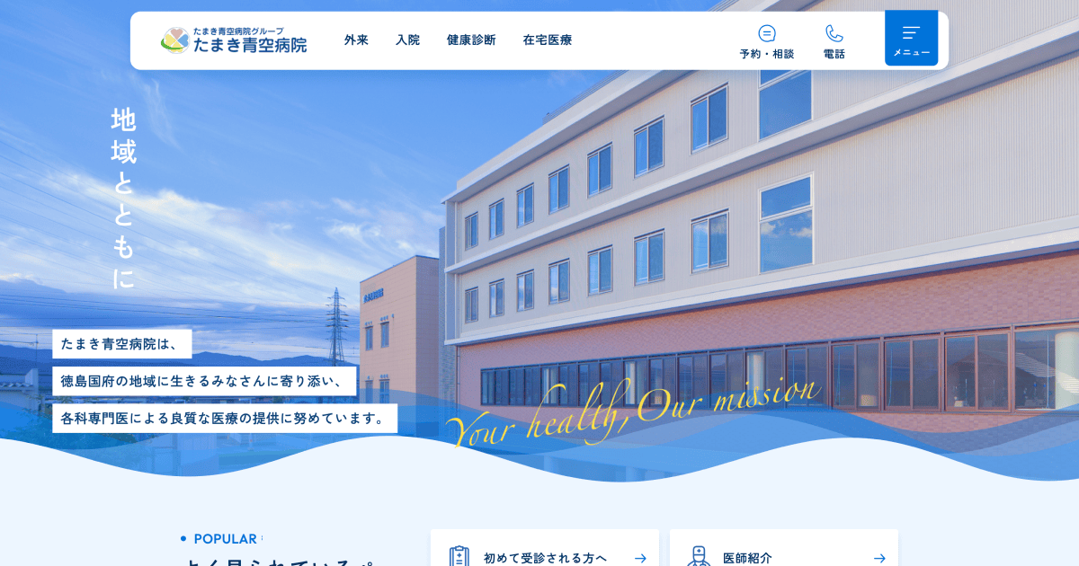 たまき青空病院（本院サイト）のファーストビュー。青空を背景にした病院外観の写真に「地域とともに」の見出しが重なり、上部に外来・入院・健康診断・在宅医療のナビゲーションと、予約・相談／電話のボタンが並んでいる